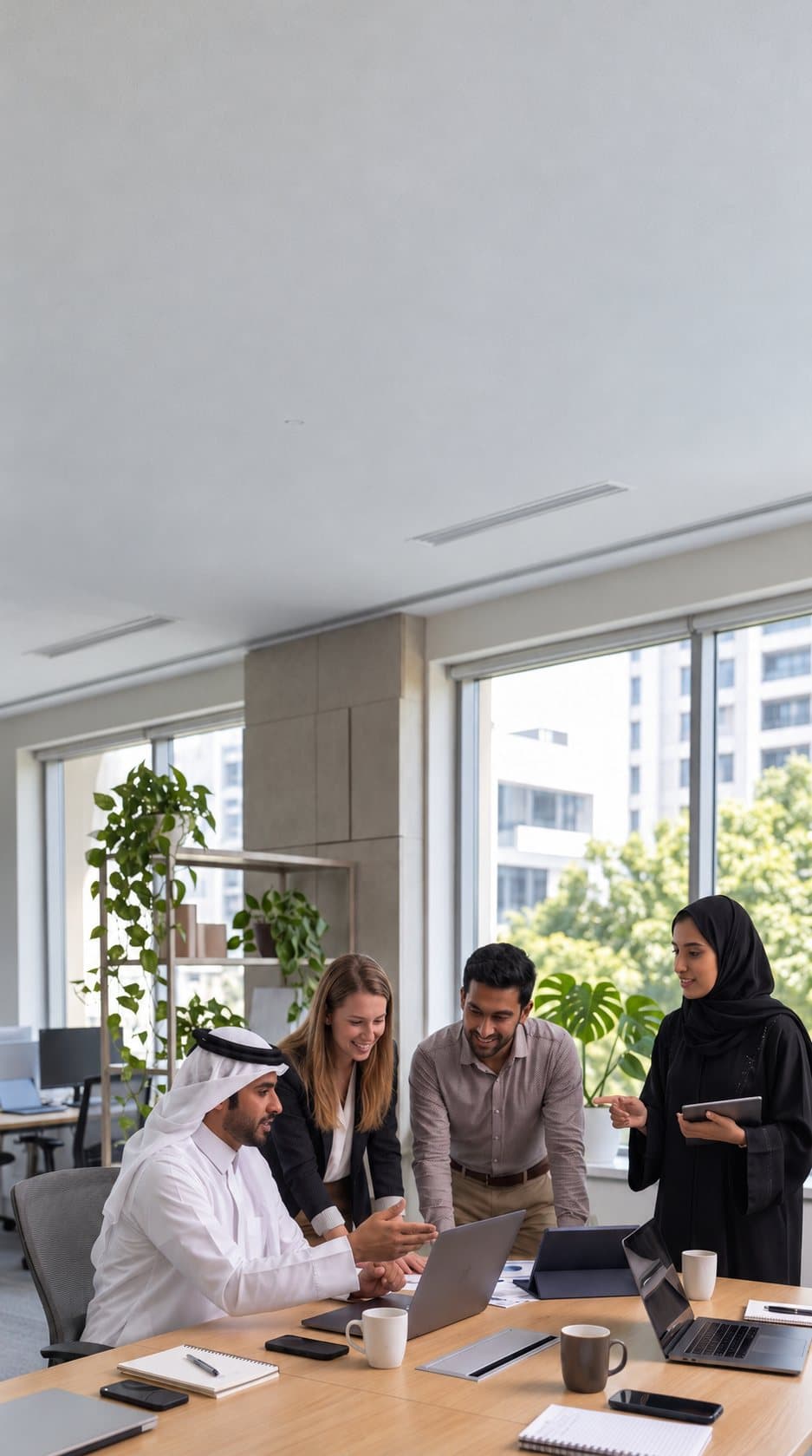 Four colleagues in a bright office gathered around a laptop and a tablet